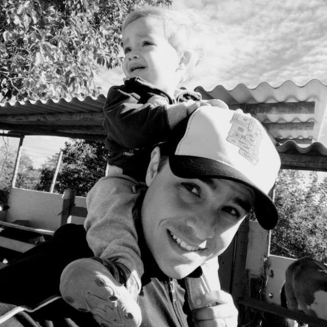 Fotografia de Rodrigo Cornelio, com um boné na cabeça e o filho nos ombros.